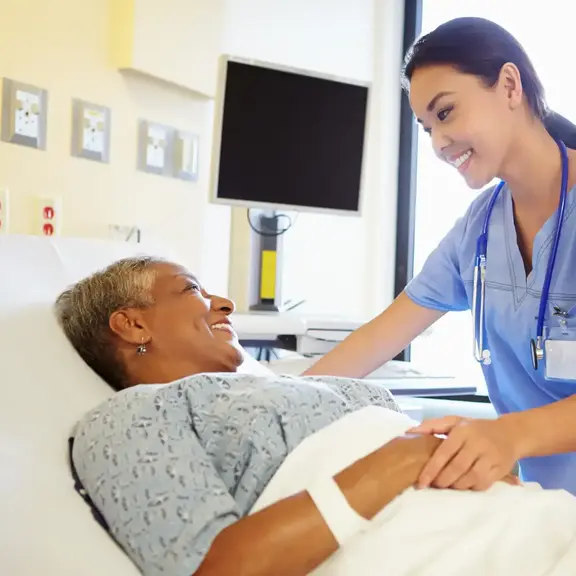 Nurse assisting an older patient in a hospital bed during recovery.
