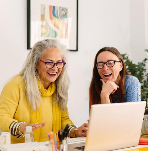 Two women working together on a computer and laughing. 