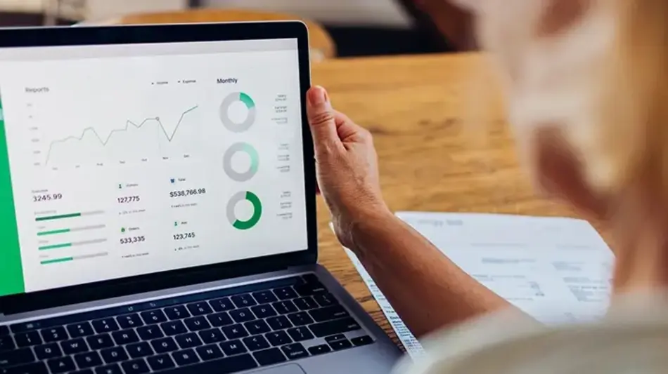 Image looking from behind an older woman's left shoulder toward her open laptop with her investments dashboard showing