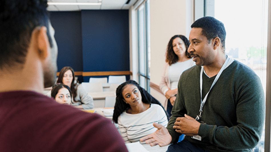 Educator speaking with a group of students in a classroom, engaging in discussion.