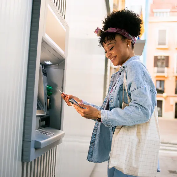 Beautiful young multiracial woman taking the money from the ATM machine for shopping.