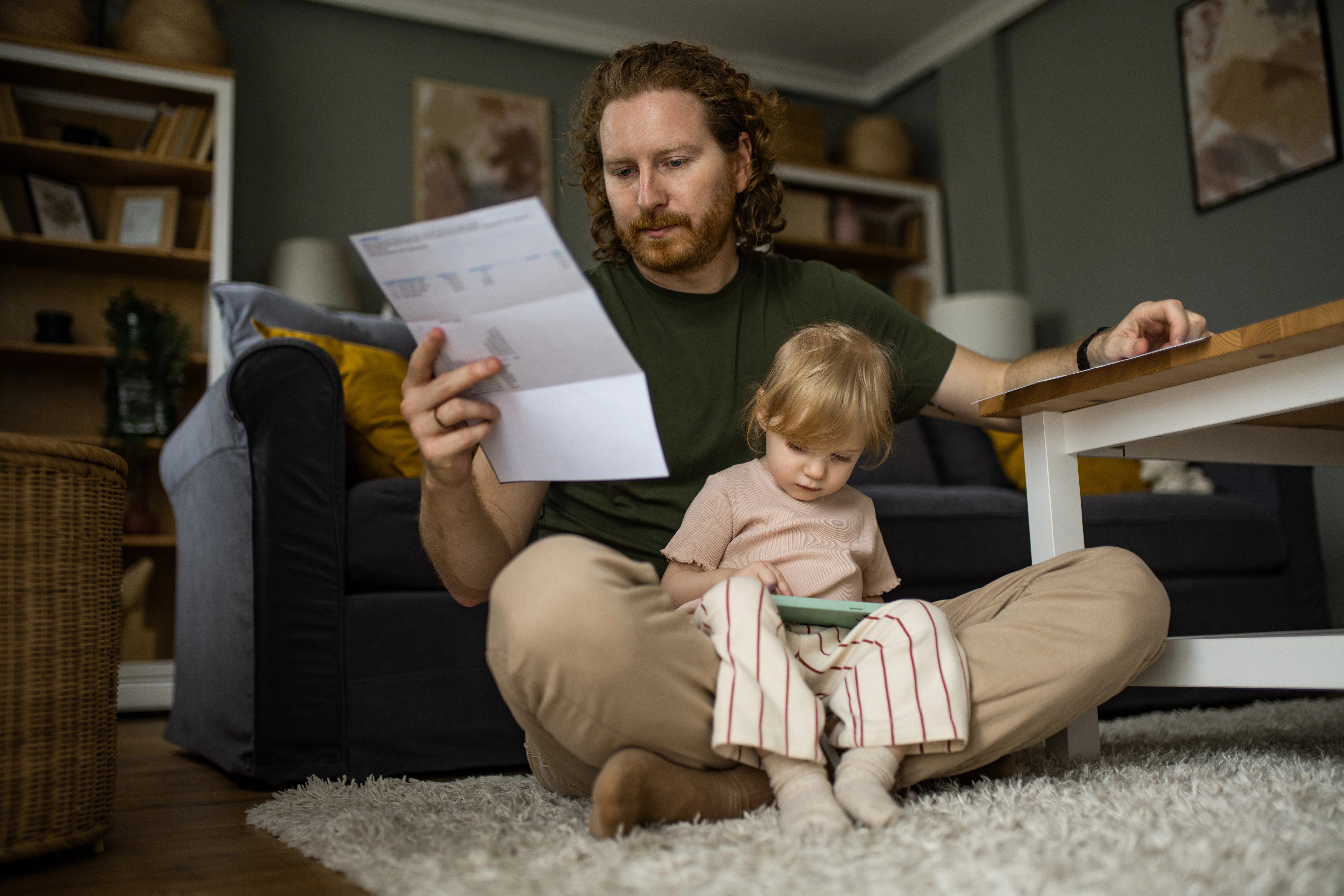 Worried father paying bills while his little daughter is sitting on his lap at home.