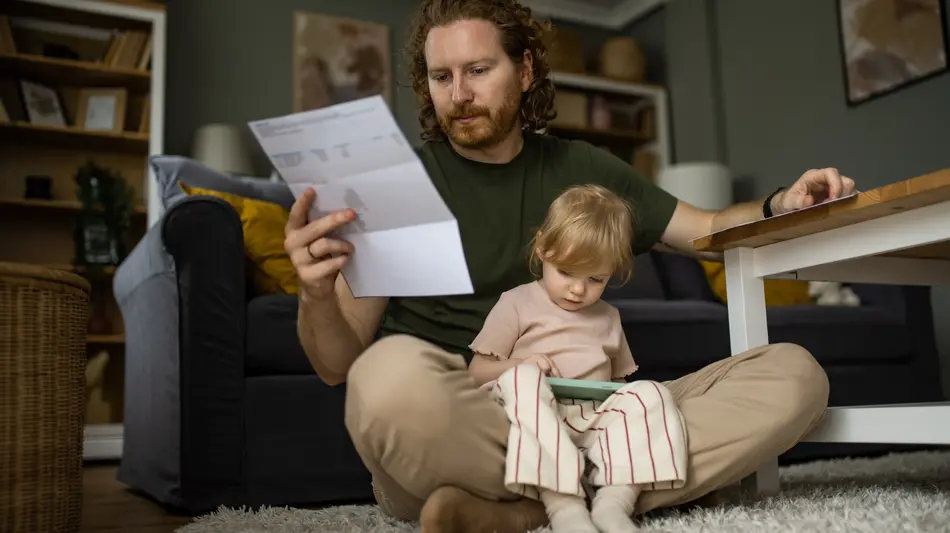 Worried father paying bills while his little daughter is sitting on his lap at home.
