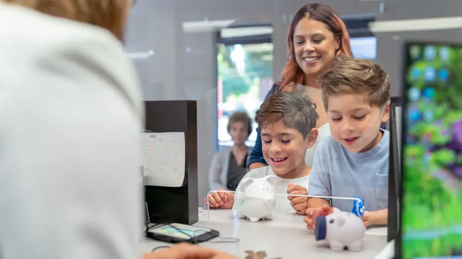 Two elementary age boys of Hispanic descent smile with excitement as a bank teller counts the coins they brought from their piggy banks.