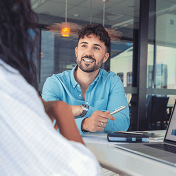 Financial advisor discussing investment performance with a client at a desk, reviewing charts and graphs on a laptop.
