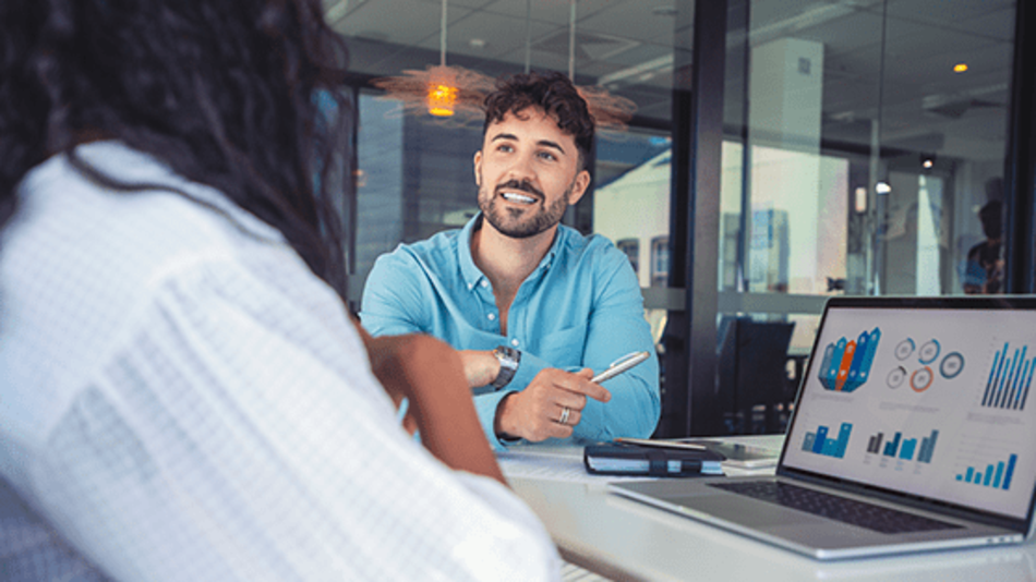 Financial advisor discussing investment performance with a client at a desk, reviewing charts and graphs on a laptop.
