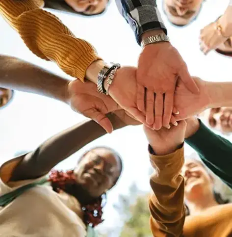 Image of people in a circle putting their hands together in the middle of the circle