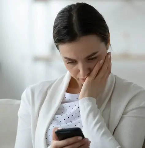 Image of woman looking concerned while resting her head on her left and while looking at the cell phone screen in her right hand