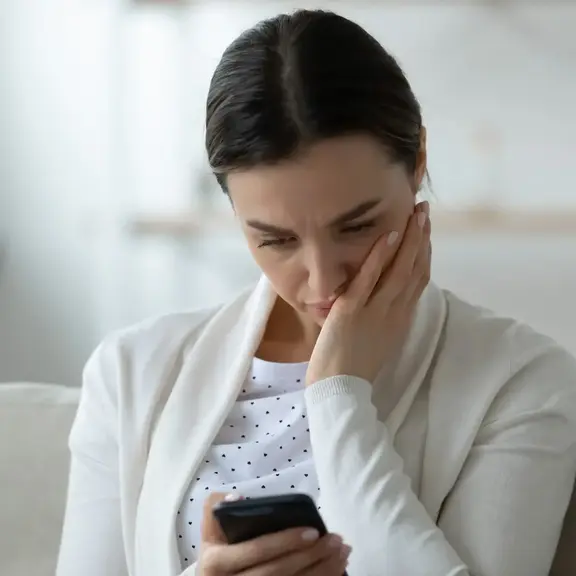 Image of woman looking concerned while resting her head on her left and while looking at the cell phone screen in her right hand